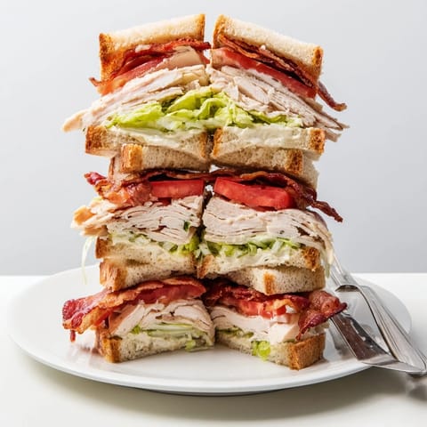 Toasted bread layers showcase a hearty Turkey Club Sandwich loaded with turkey, smoky bacon, creamy mayonnaise, and garden-fresh vegetables.