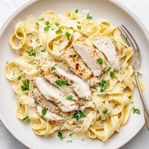Golden, tender chicken slices rest atop a plate of Fettuccine Alfredo.