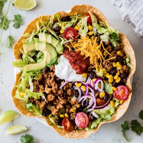 Golden baked taco salad bowl topped with creamy sour cream, chunky salsa, and diced avocado garnish. 