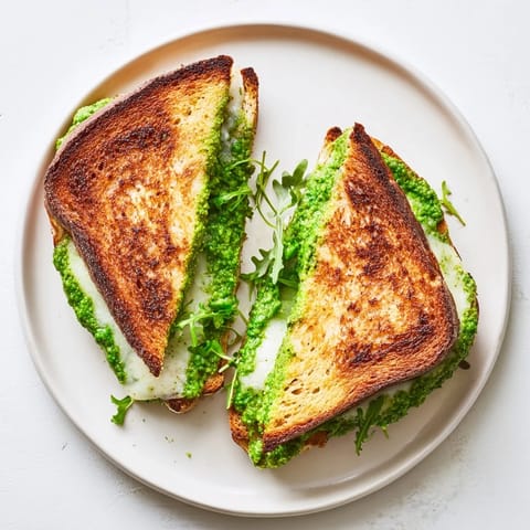 Golden, crispy sourdough slices are filled with vibrant green pea pesto and melted mozzarella cheese on a rustic cutting board.  