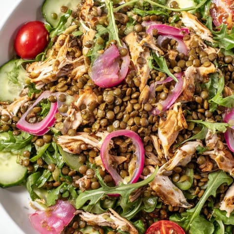 Hearty Lentil & Chicken Spring Salad served in a white bowl, showcasing bright arugula, shredded chicken, and cherry tomatoes glistening with mustard dressing.