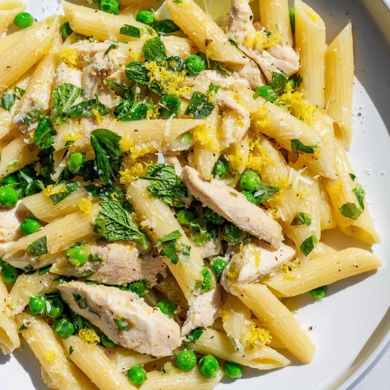 A close-up of Pea & Mint Chicken Pasta highlights fresh mint, peas, and golden chicken in a creamy lemon sauce.
