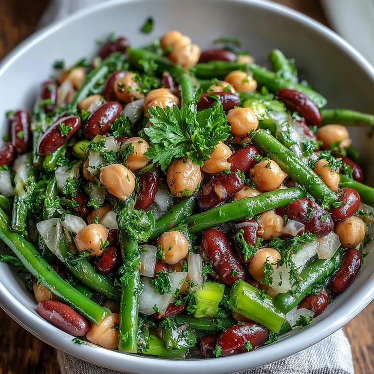 Festive Three-Bean Salad in a glass bowl, dotted with crisp celery, red onion, and parsley for a picnic-ready side.