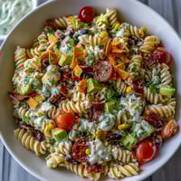 Colorful taco pasta salad with rotini, black beans, corn, and avocado, topped with shredded cheddar and a creamy taco dressing.
